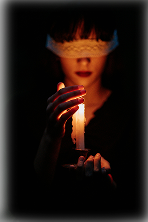 A woman in dark room, and she is blindfolded with a peice of lace fabric.